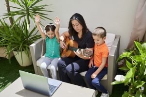 Family at home learning to play the guitar through online courses in quarantine time. Young pupils learning from mom